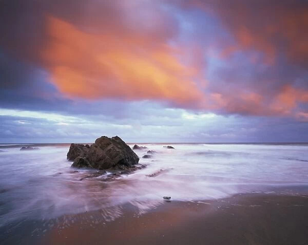 Widemouth Bay at sunrise, with offshore rocks and red storm clouds overhead