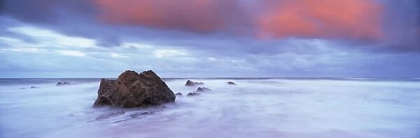 Widemouth Bay at sunrise, with offshore rocks and red storm clouds overhead