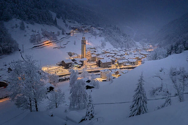 Winter dusk over the illuminated village in deep snow, Gerola Alta, Valgerola