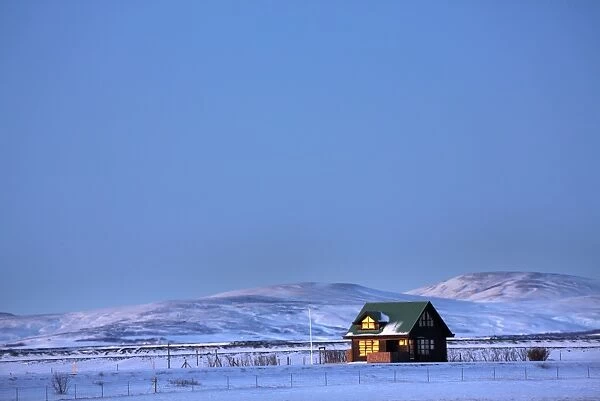 Winter landscape at dusk showing lone cabin bathed in evening sunlight, near Seljalandsfoss