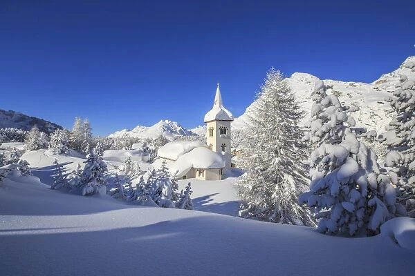 The winter sun illuminates the snowy landscape and the typical church, Maloja, Engadine
