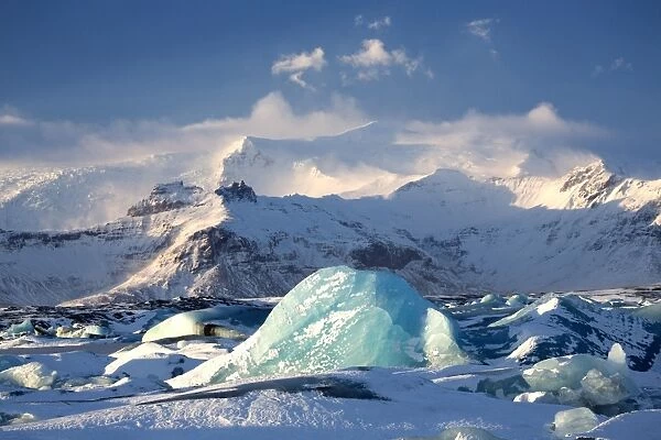 Winter view over frozen Jokulsarlon Glacier Lagoon showing blue icebergs covered in snow