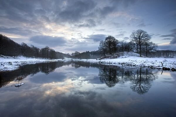 Winter view of River Brathay at dawn, under snow with reflections, near Elterwater Village