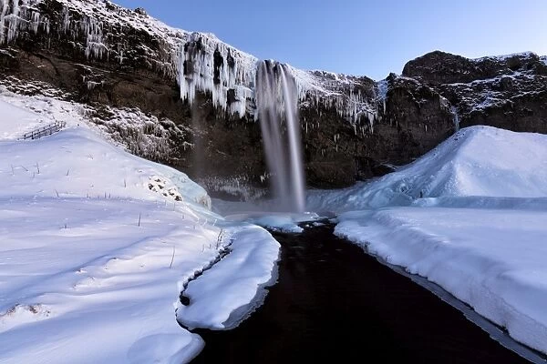Winter view of Seljalandsfoss Waterfall at dusk with snow covered foreground