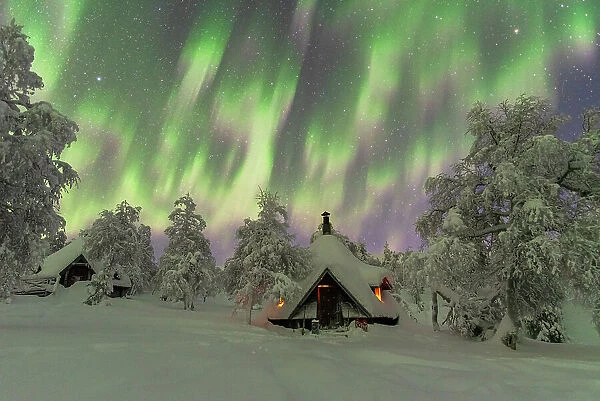 Winter view of a typical wooden hut lit by the fire in the frozen wood during a Northern Lights (Aurora Borealis) storm, Finnish Lapland, Finland, Europe