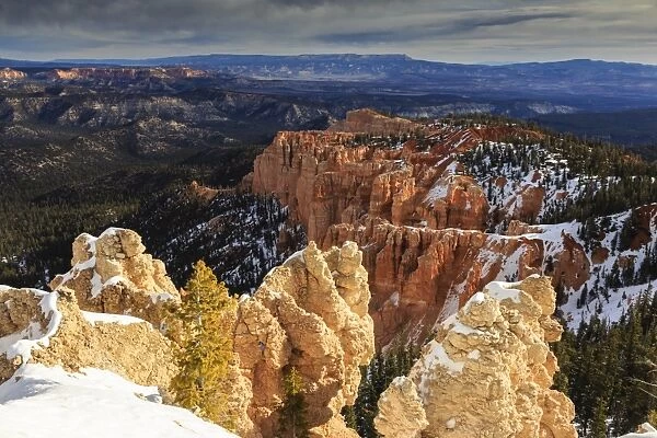 Wintry cliffs and hoodoos strongly lit by morning sun with cloudy backdrop, Rainbow Point, Bryce Canyon National Park, Utah, United States of America, North America