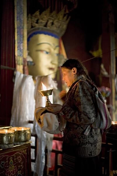Woman adding yak butter from her butter lamp to those in the Buddhist temple