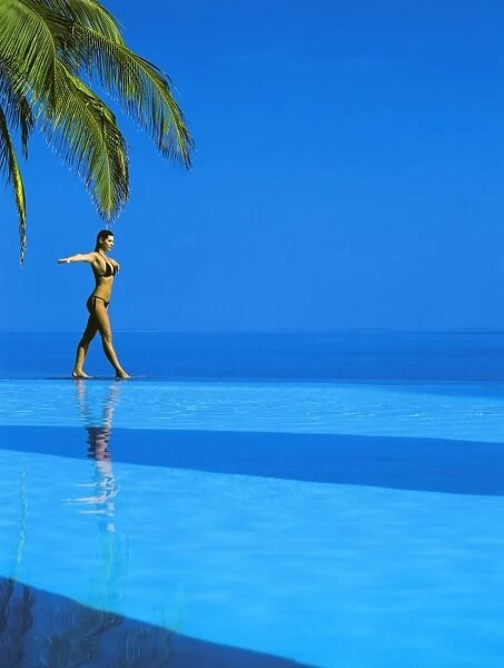 Woman balancing on edge of infinity pool, Maldives, Indian Ocean, Asia