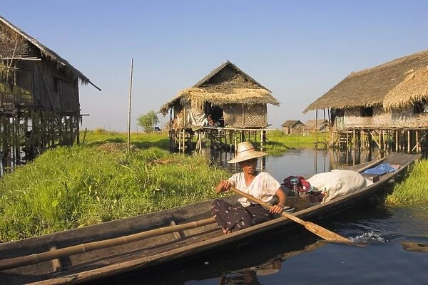 Woman in canoe paddles past floating village, Inle Lake, Shan State, Myanmar (Burma)