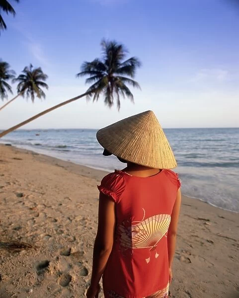 Woman in conical hat walking along the beach