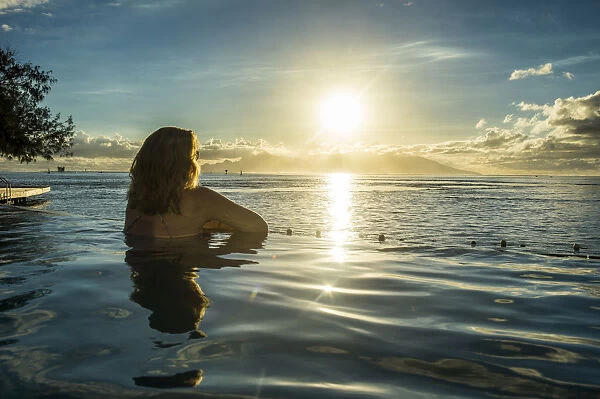 Woman enjoying the sunset in a swimming pool with Moorea in the background, Papeete