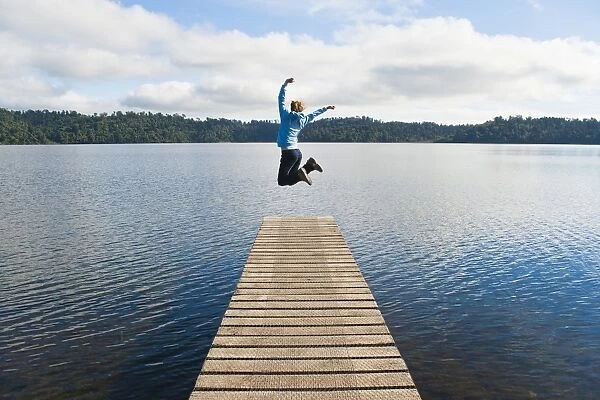 Woman jumping on a jetty at Lake Ianthe, West Coast, South Island, New Zealand, Pacific