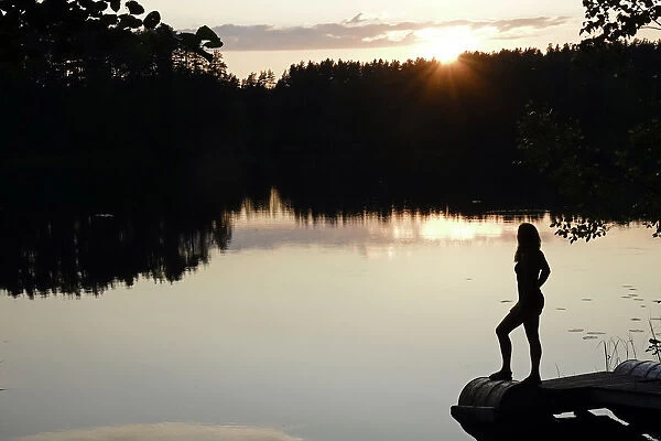 Woman looking out across a lake in rural Finland, Scandinavia, Europe