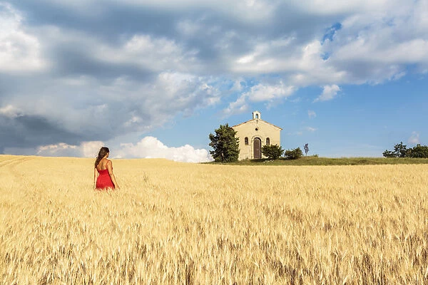 Woman in red dress admiring Notre-Dame-de-Sante chapel in a wheat field, Entrevennes