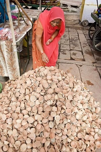Woman in red sari with pile of terracotta deepak candle dishes for Diwali festival celebrations
