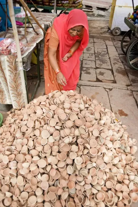 Framed Print : Woman in red sari with pile of terracotta deepak candle dishes for Diwali festival celebrations