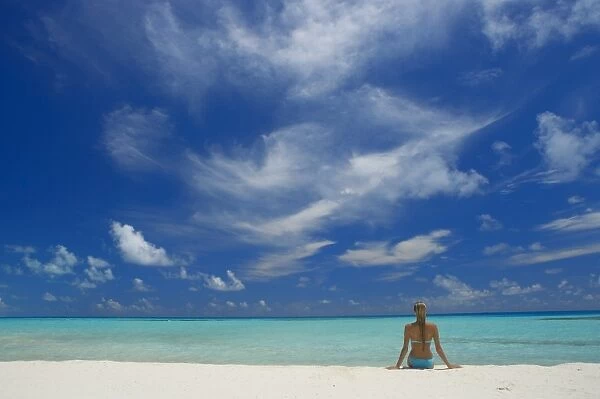 Woman sitting on the beach looking out to sea, Maldives, Indian Ocean, Asia