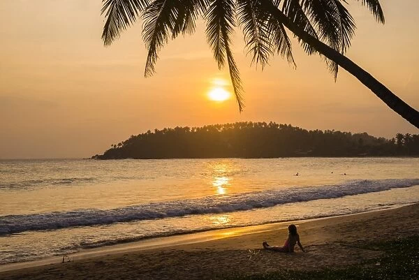Woman sitting on Mirissa Beach watching the sun set, South Coast of Sri Lanka, Southern Province, Sri Lanka, Asia