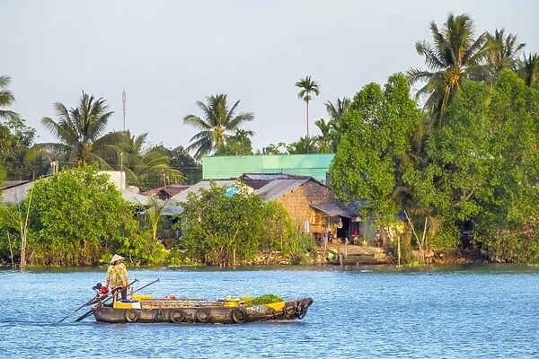 A woman in a small boat passes a village on the Can Tho River, a branch of the Mekong River
