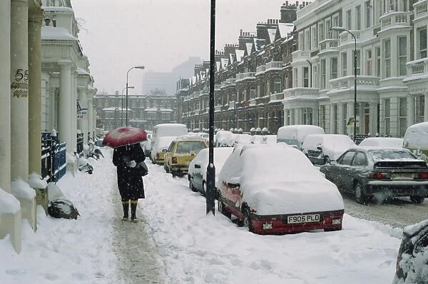 Woman with umbrella and cars covered in snow in winter in West Kensington