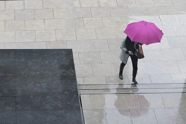 Woman with umbrella and mobile phone walking up steps to Auckland Art Gallery, Auckland