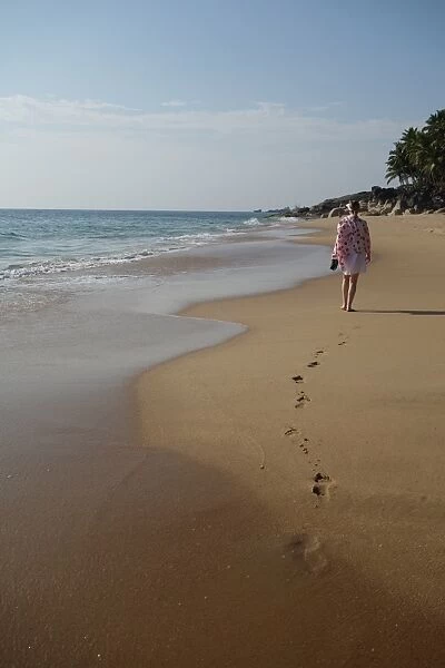 Woman walking leaving footprints on deserted beach, Niraamaya, Kovalam, Kerala, India
