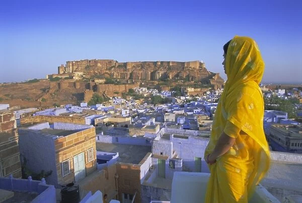 A woman in a yellow sari looking out over the Blue city and fort