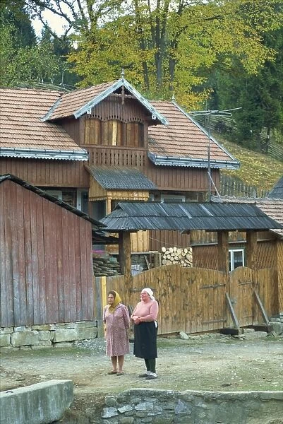 Two women stand in front of a house typical of the rural architecture of the region