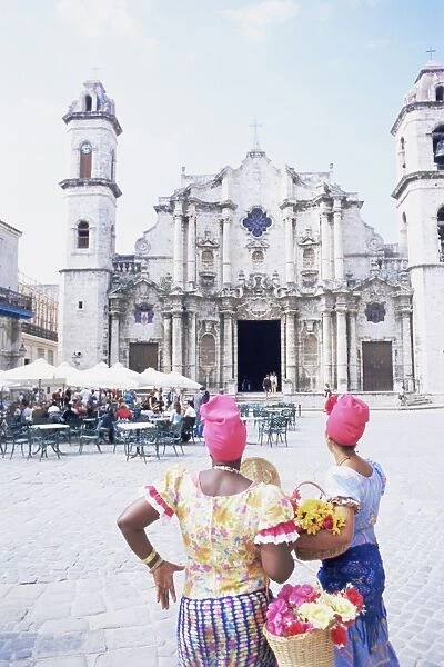 Two women in traditional clothing looking at San Cristobal cathedral, Havana