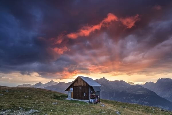 Wooden hut framed by fiery sky and clouds at sunset, Muottas Muragl, St