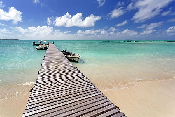 Wooden jetty with boats tied to it stretching out into the Indian Ocean off an idyllic beach on Ile Aux Cerfs, Mauritius, Indian Ocean, Africa