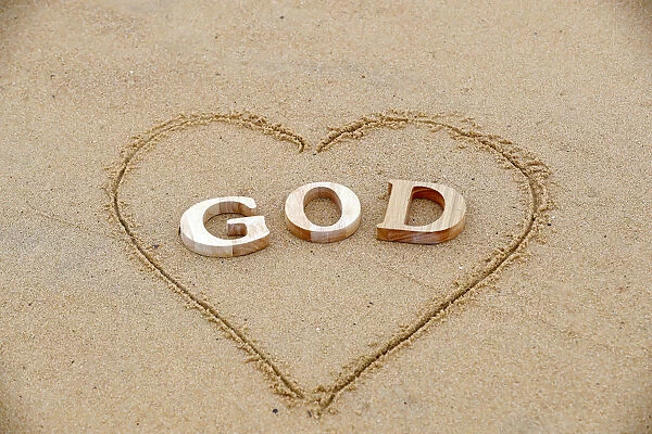 Wooden letters forming the word GOD with heart on a background of beach sand