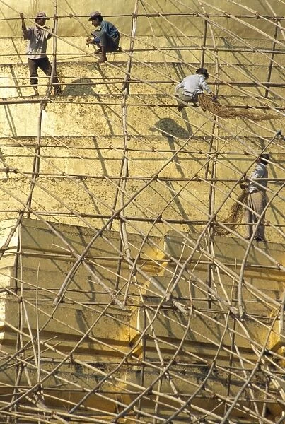 Workers on bamboo scaffolding applying fresh gold leaf to the Shwedagon Pagoda