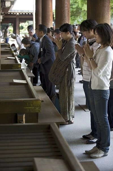 Worshippers praying in front of offertory boxes at main hall of Meiji Jingu shrine in Tokyo