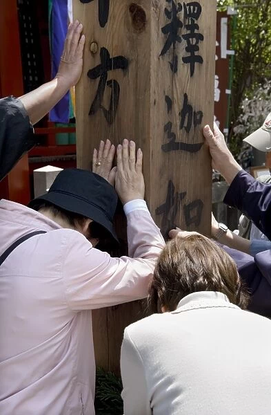 Worshippers touching a wooden obelisk for inspiration at a sub temple of Zenkoji Temple