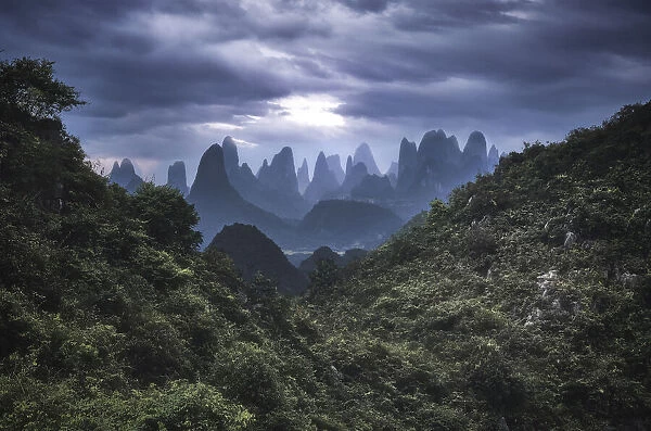 Yangshuo mountains with dark clouds framed by hills, Yangshuo, Guangxi, China, Asia