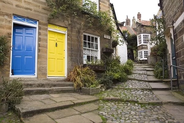 Yellow and blue doors on houses in The Opening, a narrow stepped cobbled alley on steep hill in Old Bay part of the fishing village, Robin Hoods Bay, Yorkshire, England, United