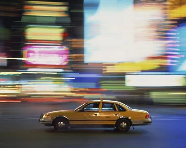 Yellow cab driving past blurred neon lights at night in Times Square in New York
