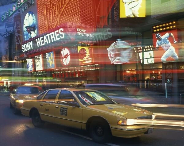Yellow cabs on the street at night with neon lights of Sony Theatres in the background