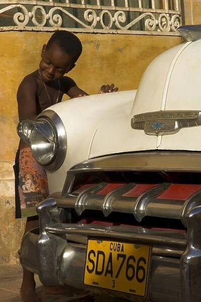 Young boy drumming on old American cars bonnet, Trinidad, Sancti Spiritus province, Cuba, West Indies, Central