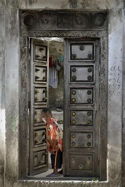Young little boy looking through a old wooden door, Moroni, Comoros, Africa