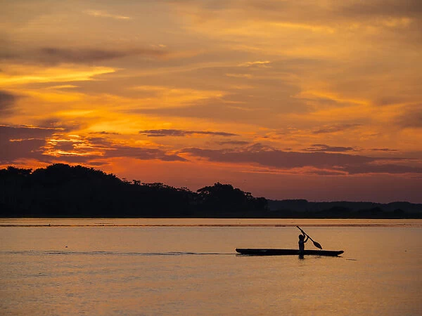 Young man paddling his fishing boat at sunset over calm waters on Clavero Lake, Amazon
