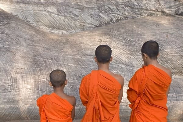 Three young monks praying at a rock-cut image of the
