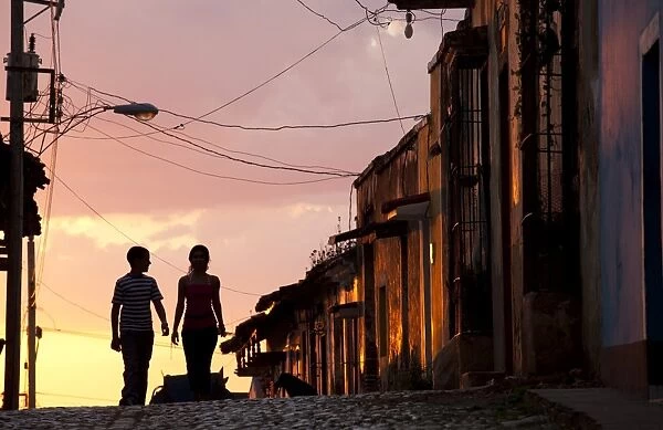 Two young people in silhouette at sunset on cobbled street with colourful orange sky behind, Trinidad, UNESCO World Heritage Site, Cuba, West Indies, Central America