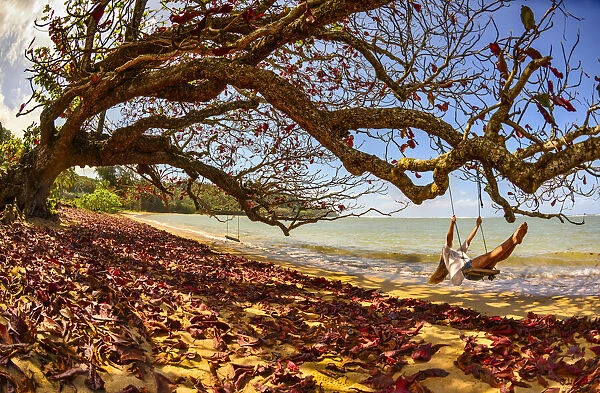 A young woman enjoys a quiet fall day by the seaside on a swing, Kiluea, Hawaii