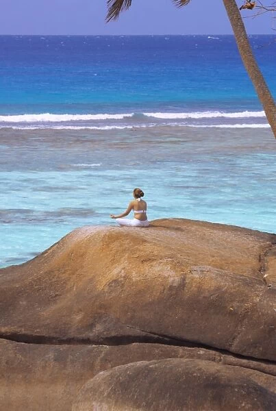 Young woman meditating on rock, Seychelles, Indian Ocean, Africa