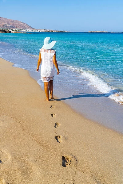 Young woman with sundress and hat walking on sand beach, Crete island, Greek Islands