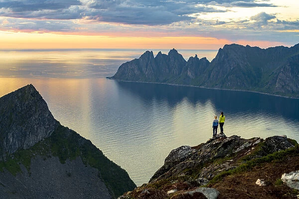 Two young women watching sunset standing on mountain top, Senja island, Troms county