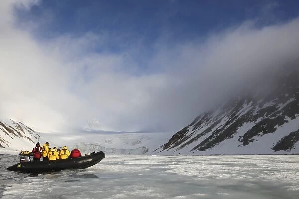 Zodiac inflatable with tourists exploring Arctic landscape in summer sunshine