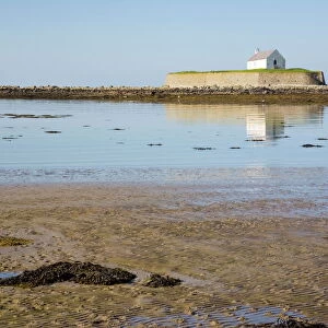 The 12th century Llangwyfan church on small tidal island reflected in calm sea